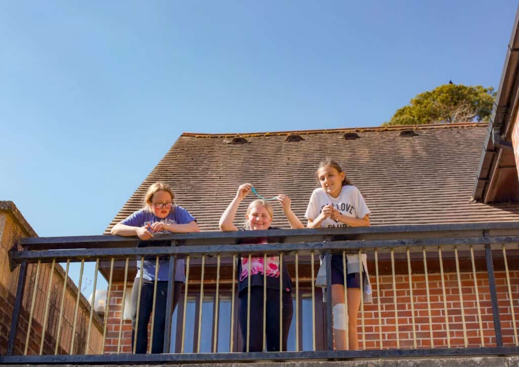 Three happy girls leaning on a shaded balcony at Educamps, laughing together as one proudly shows off the colourful slime she made during a summer craft activity. Sheltered from the sun but still soaking in the vibrant camp atmosphere, they’re enjoying a perfect mix of creativity, friendship, and fun at our kids’ summer camp.