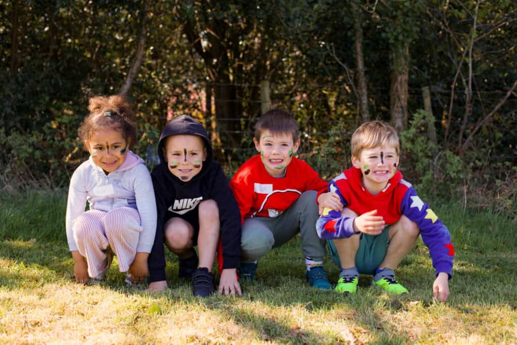 A group of excited kids showing off their colourful face paint while relaxing in the cool shade of the trees at Thorney Hill, one of our beautiful Educamps locations. Surrounded by nature, they’re enjoying a peaceful break from the summer sun after a morning full of fun activities and outdoor adventures.