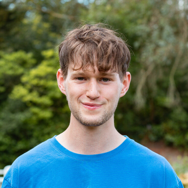 Educamps day camp leader Alex smiling outdoors in a blue camp t-shirt, supporting fun children’s activities in nature.